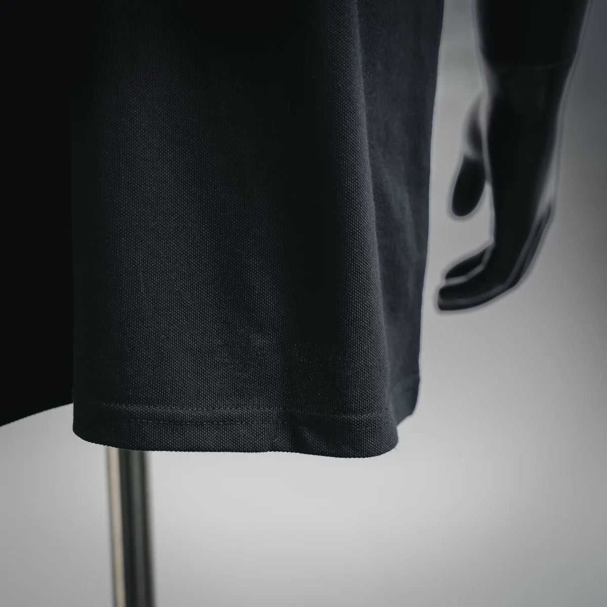 Black polo shirt sleeve and hem with visible stitching on mannequin