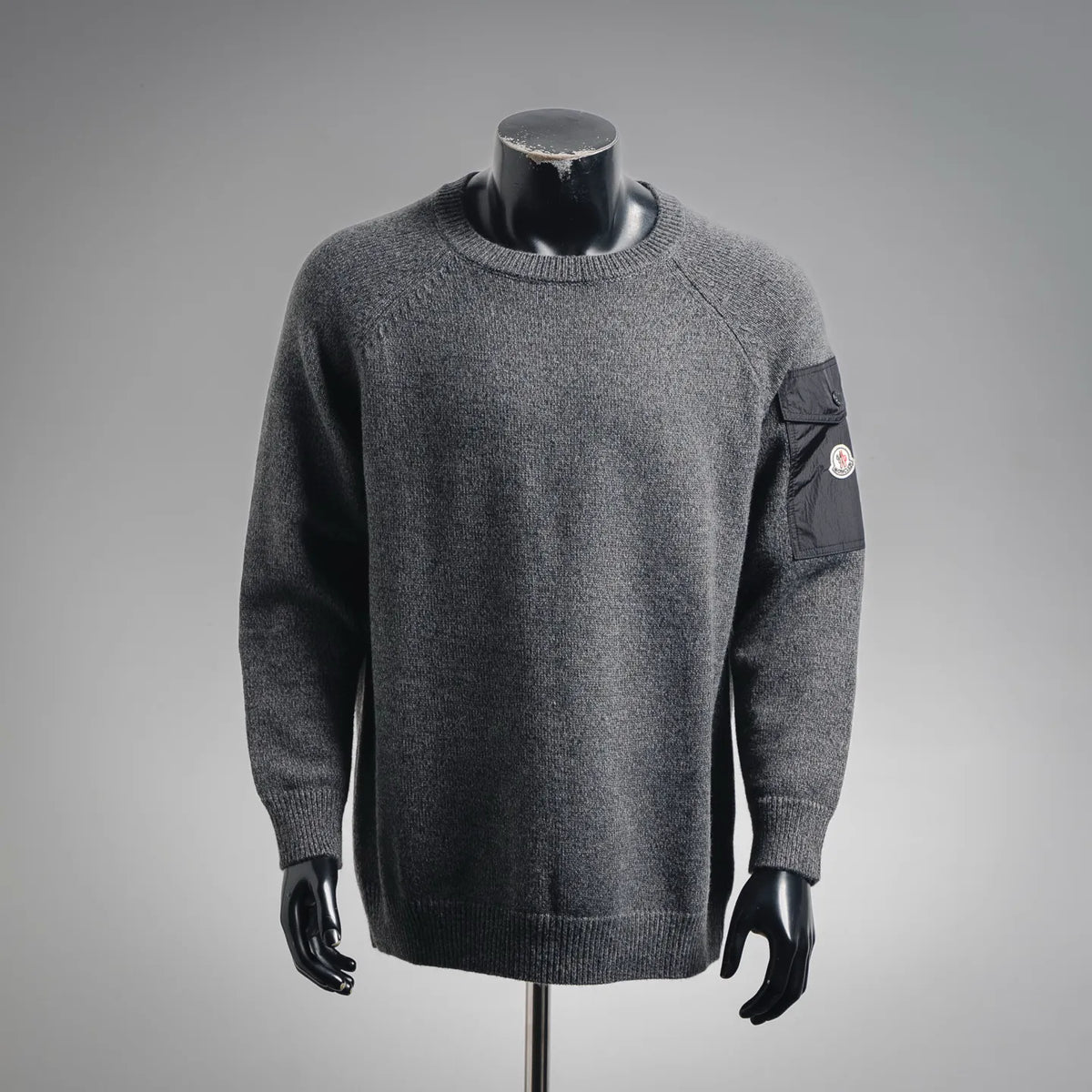 Gray heather long-sleeve knit sweater with crew neck, ribbed cuffs, and a sleeve logo patch pocket
