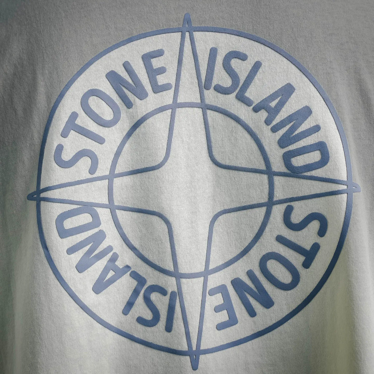 Close-up of Stone Island circular logo print on light cream T-shirt fabric