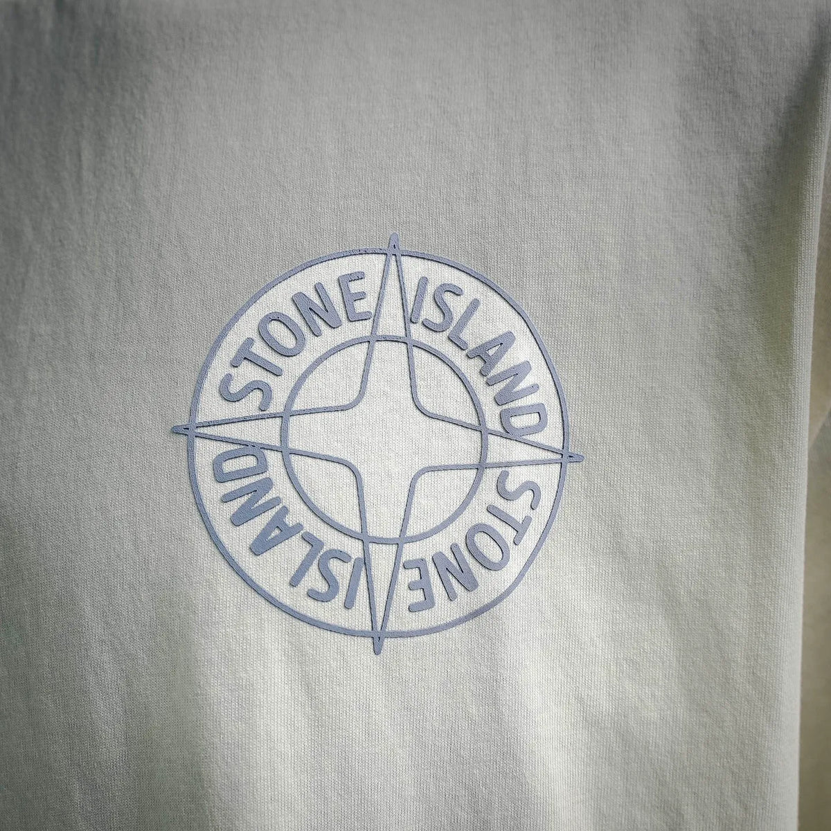 Stone Island circular logo print centered on light cream T-shirt