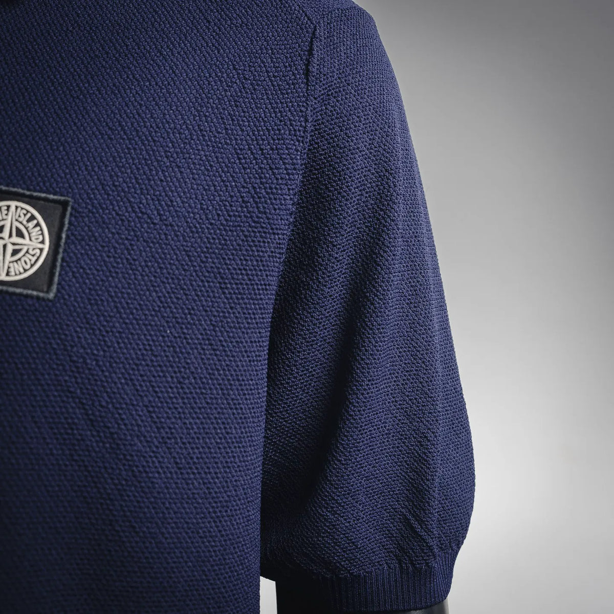 Navy polo shirt sleeve with small Stone Island-style rectangular logo patch