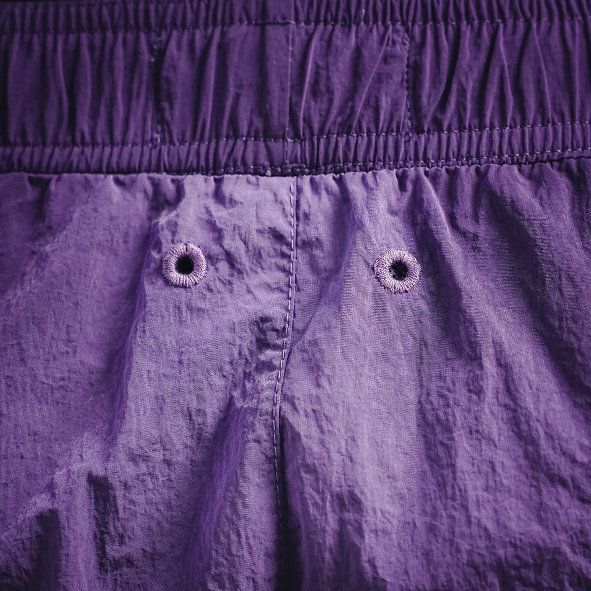 Purple Stone Island shorts front with elastic waistband and two button closures.