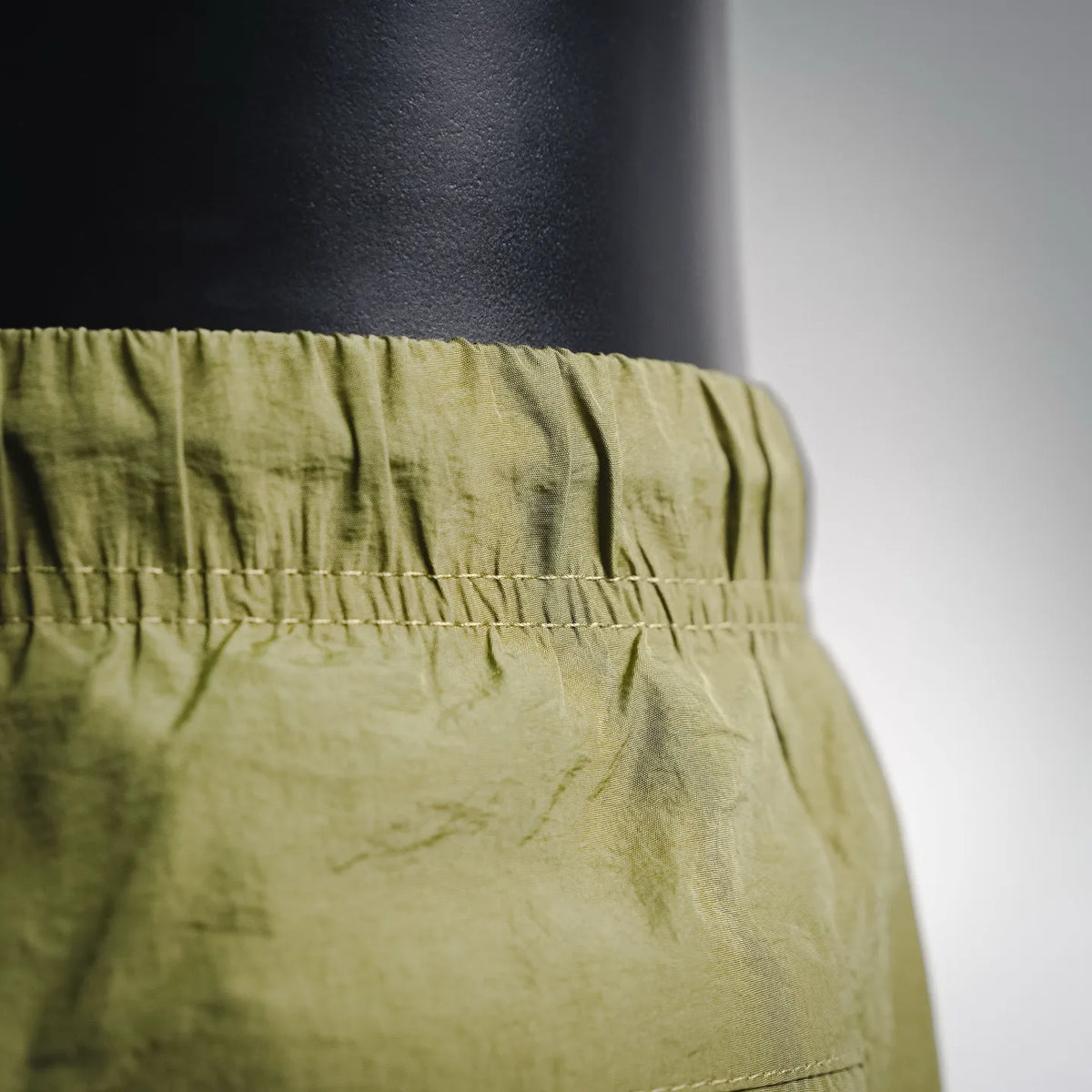 Olive green shorts elastic waistband with visible stitching and pleated panel
