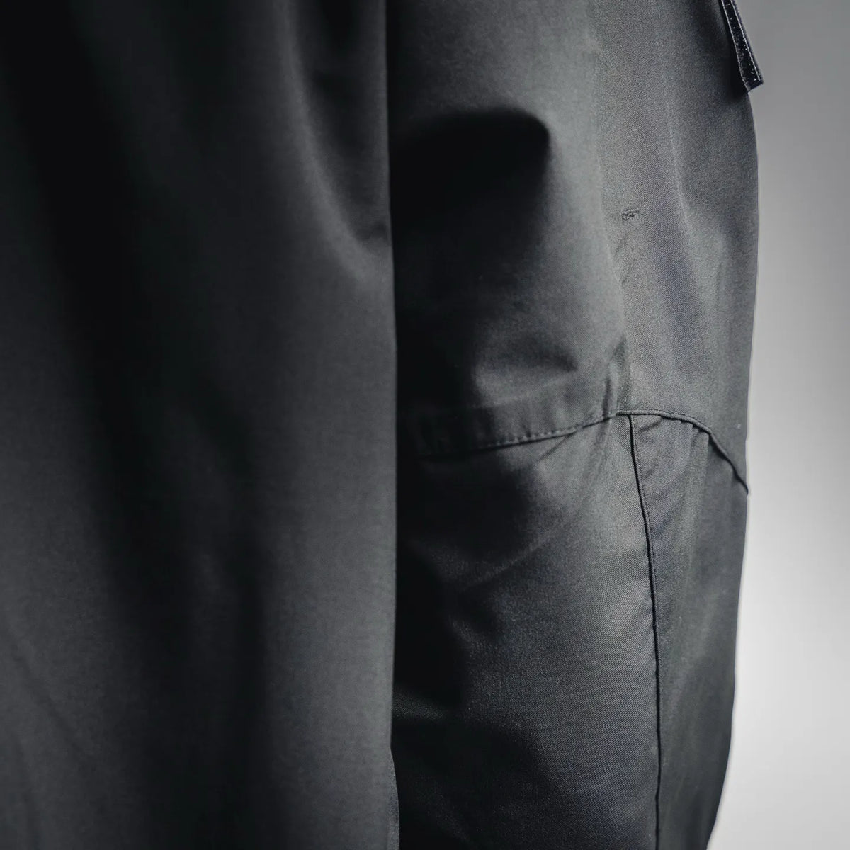Dark charcoal coat panel with stitched seam and lower pocket detail