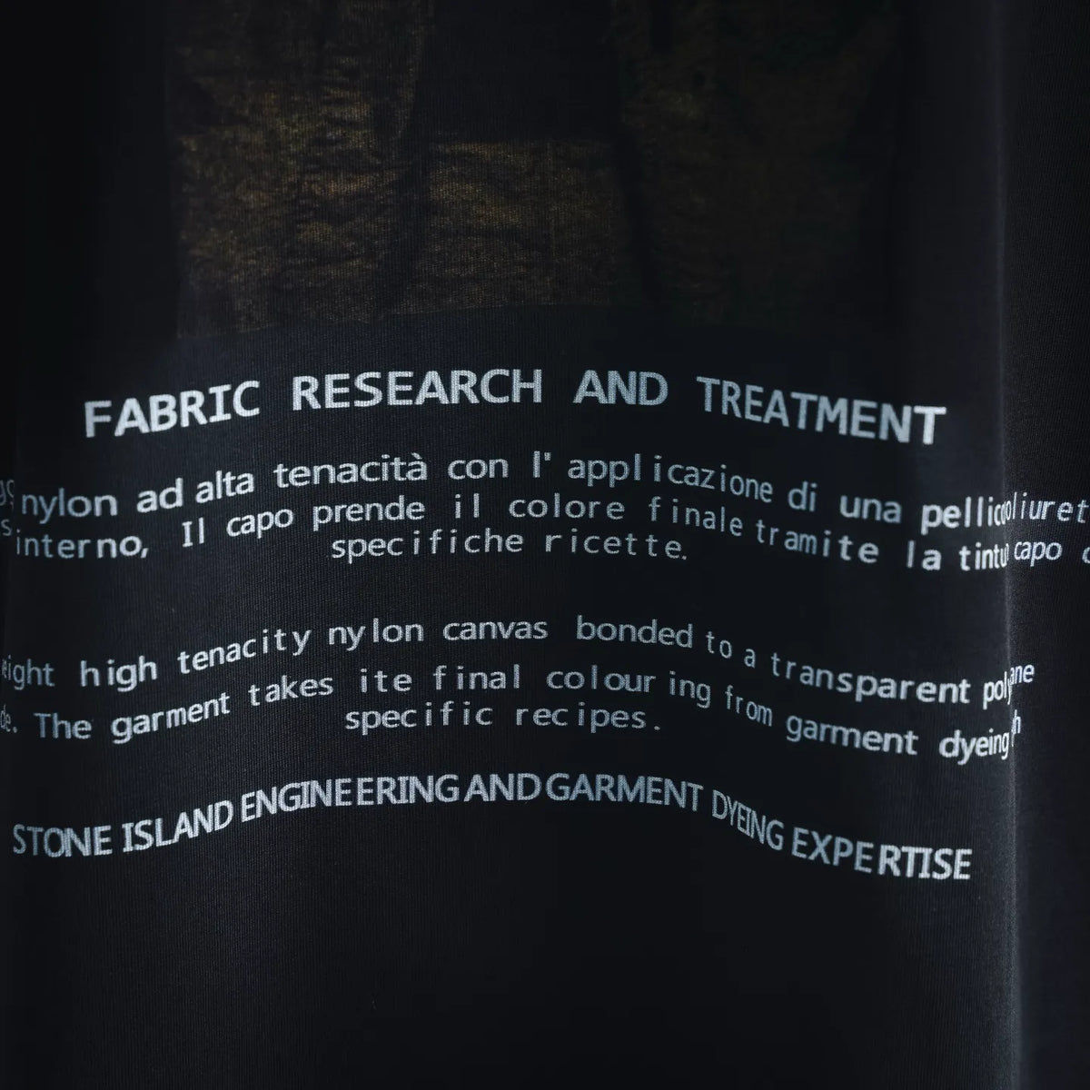 Graphic T-shirt close-up of “FABRIC RESEARCH AND TREATMENT” text on dark fabric