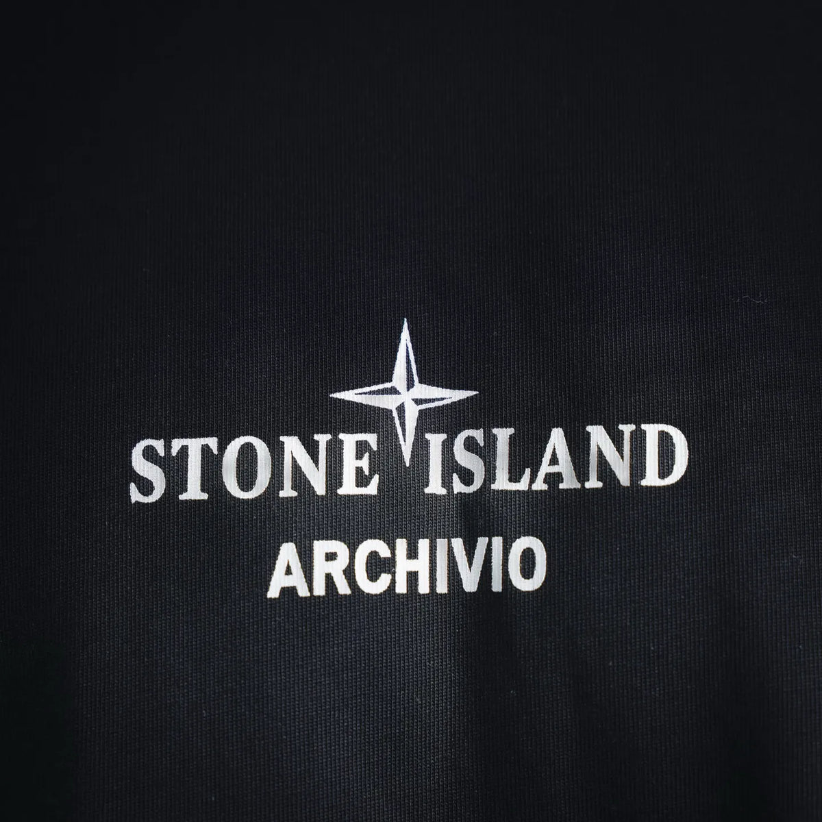 Graphic T-shirt front logo reading “STONE ISLAND ARCHIVIO” on dark fabric