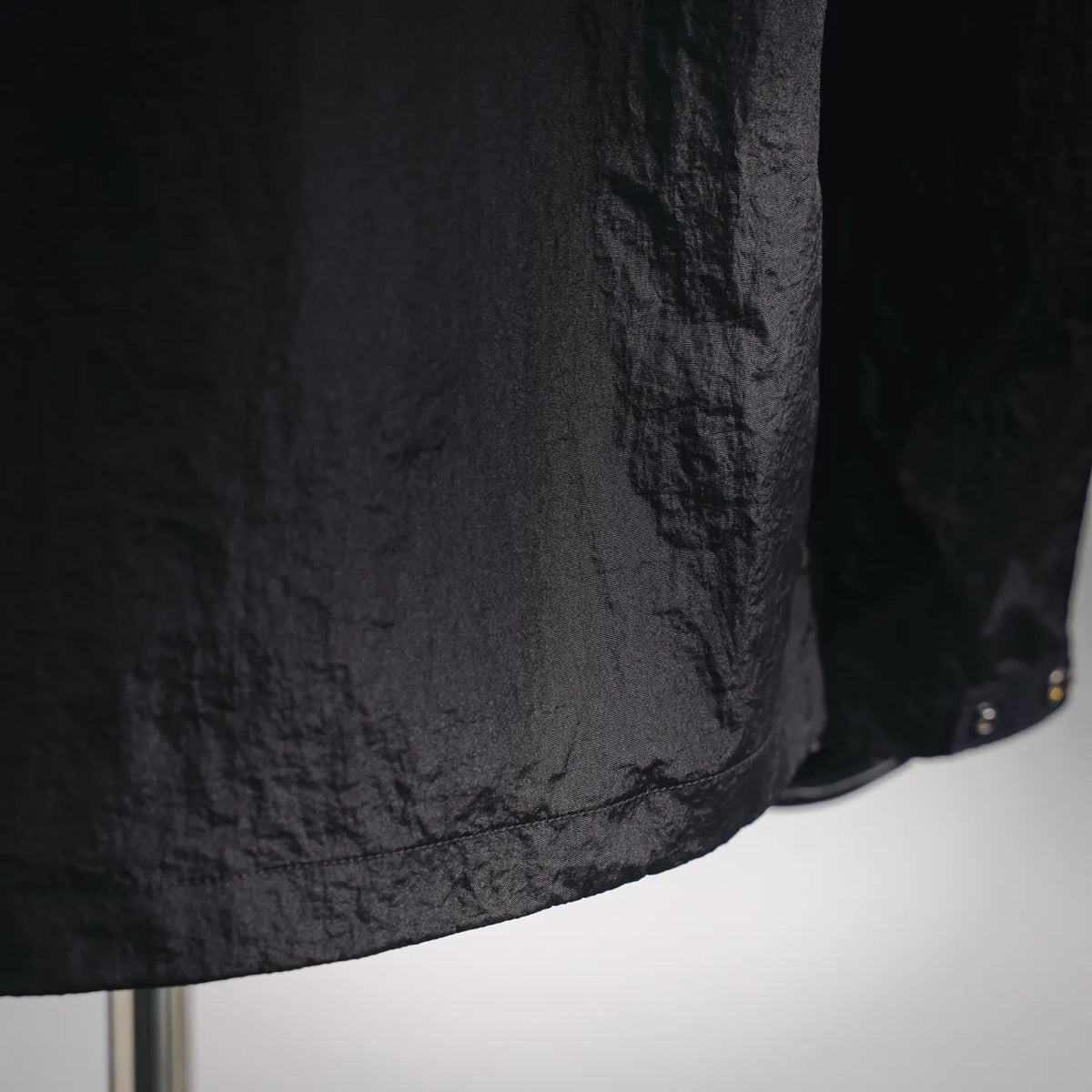 Stone Island dark coat jacket hem detail with textured finish and stitched panel.