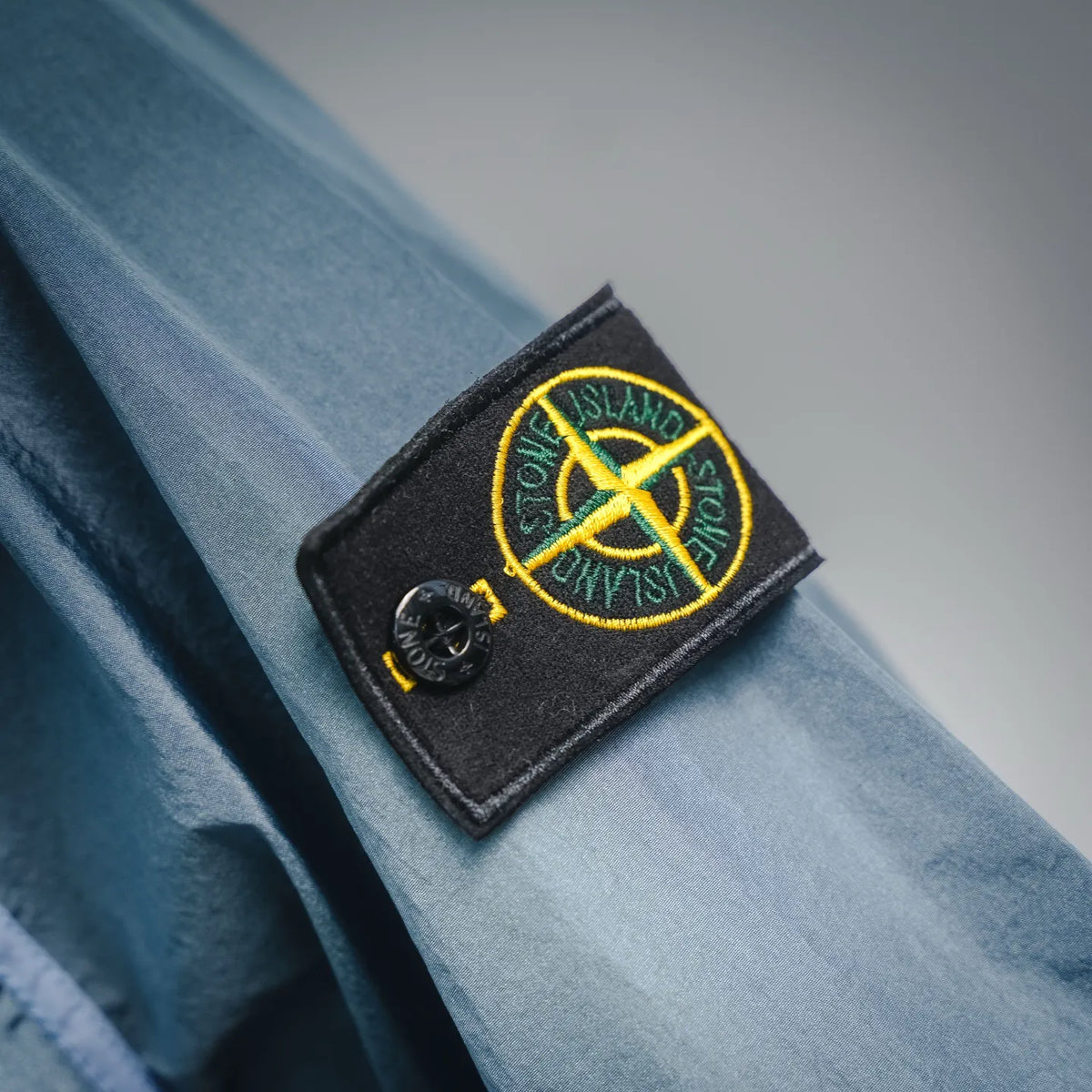 Light blue coat sleeve with black patch and yellow Stone Island logo