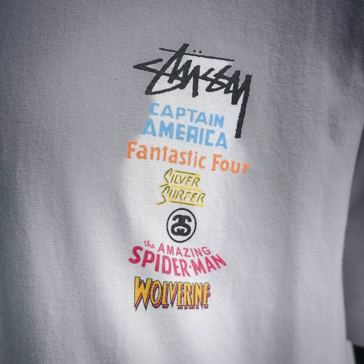 White T-shirt front graphic with Stussy logo and multicolor character text