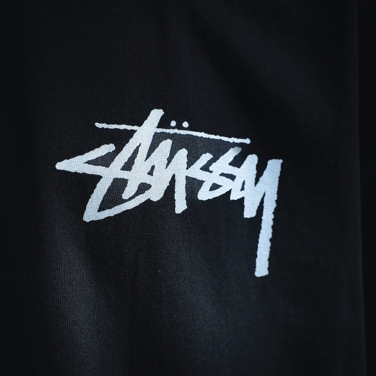 Black short-sleeve T-shirt close-up of the white Stussy chest logo.