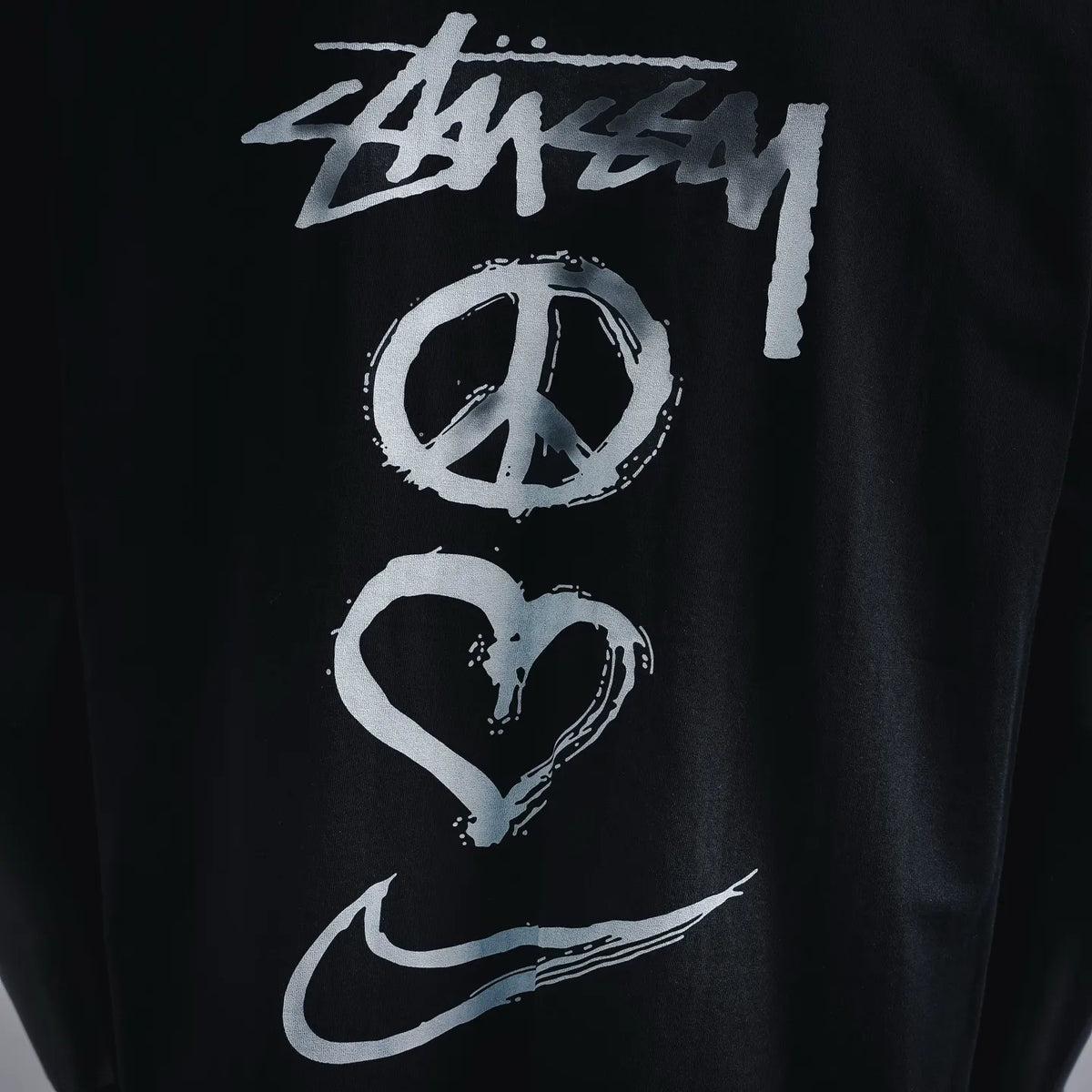 Black T-shirt graphic print close-up with Stussy logo, peace sign, and heart