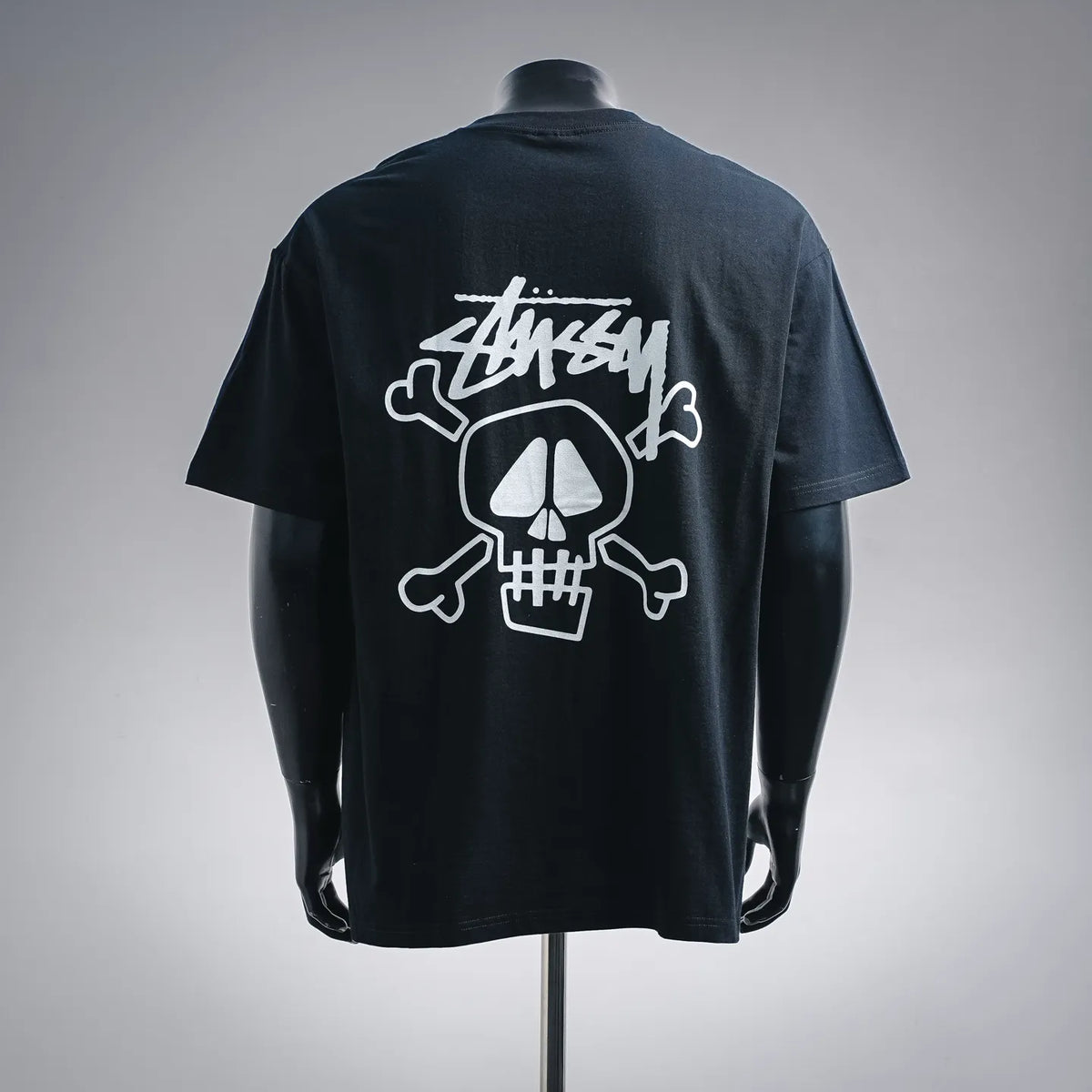 Black Stussy T-shirt with white skull-and-crossbones graphic on back