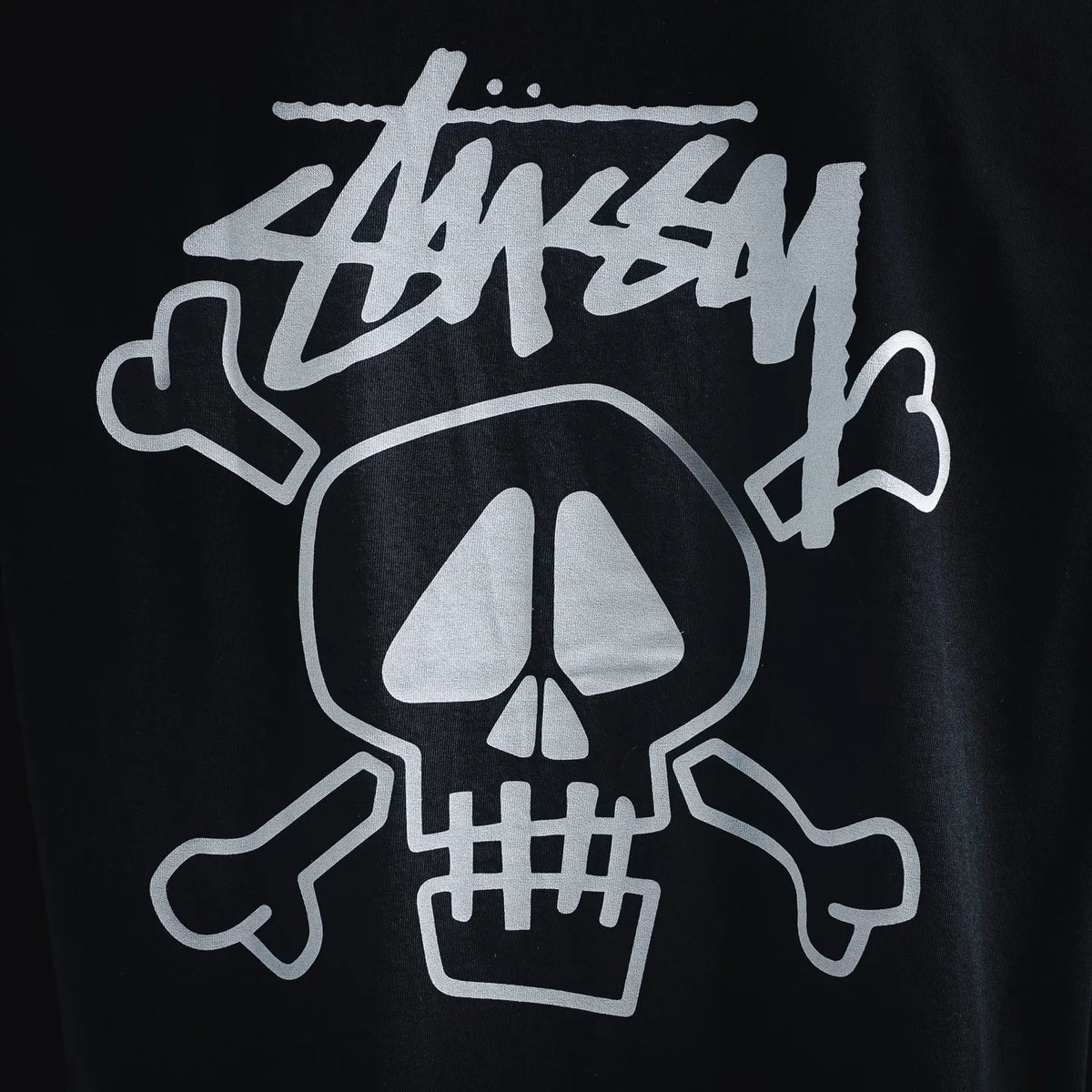 Black Stussy T-shirt close-up of white skull graphic with crossed bones