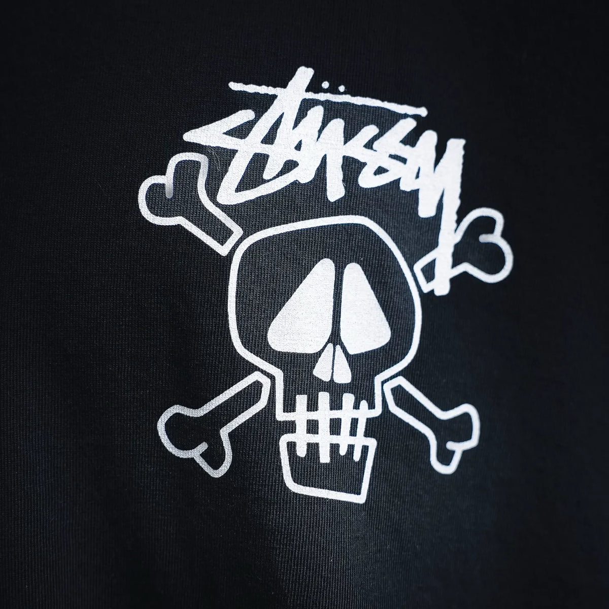 Black Stussy T-shirt close-up of white skull logo graphic