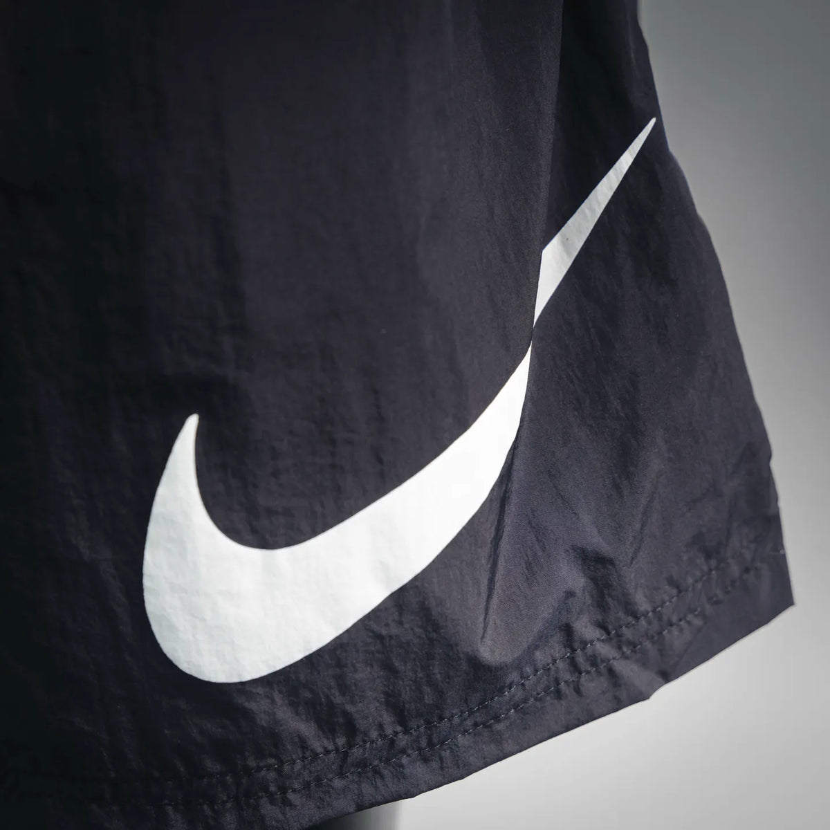 Stussy black shorts with large white Nike swoosh logo on lower leg