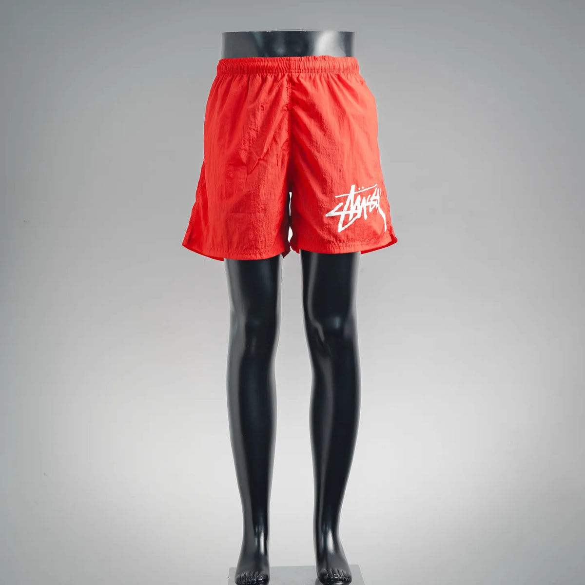 Red athletic shorts with elastic waistband and Stussy logo on the right leg