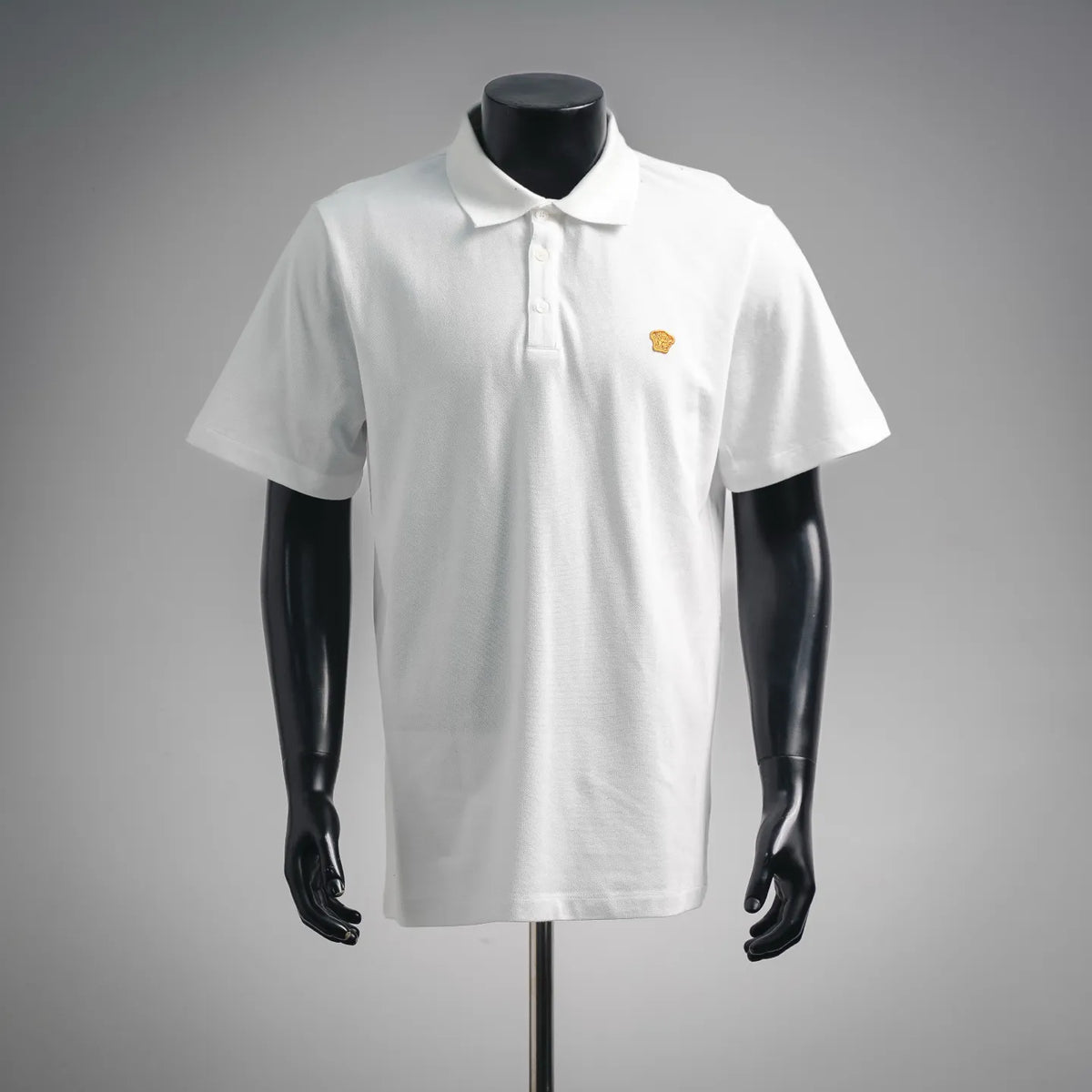 White polo shirt with short sleeves, button placket, and small gold logo on chest