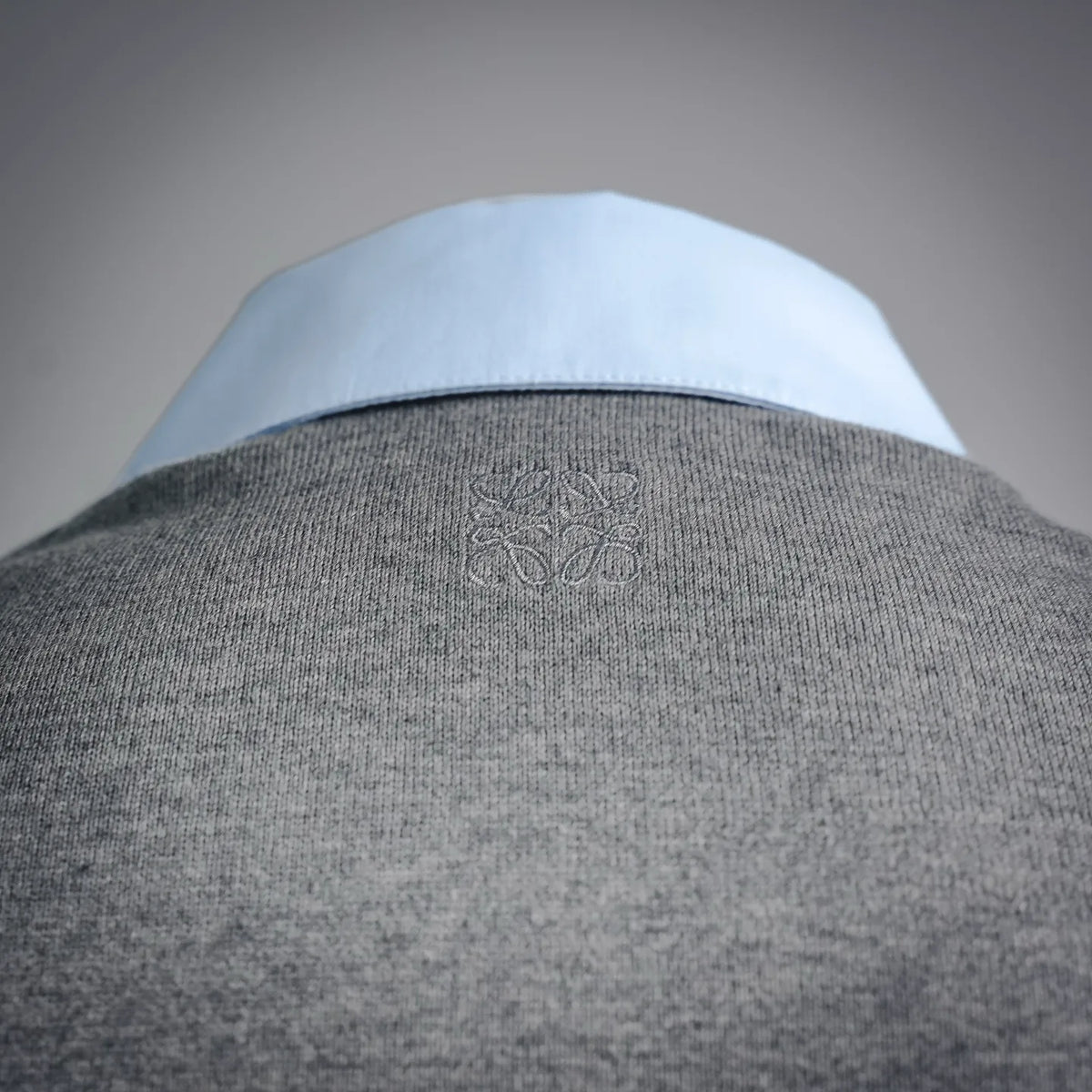 Grey knit shirt yoke with subtle embossed crest near neckline