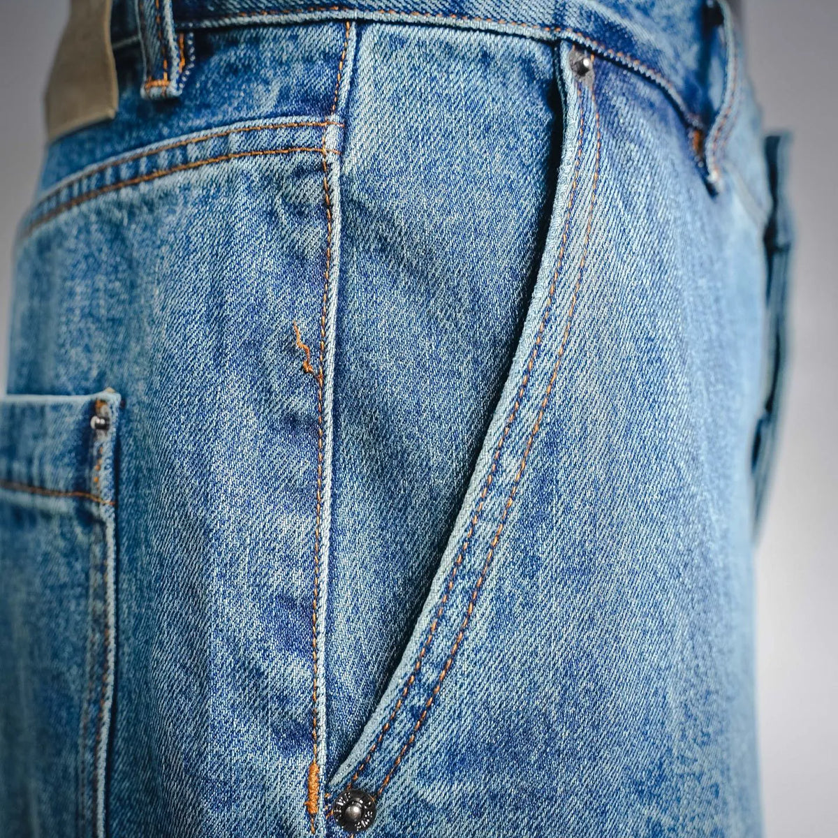 LOEWE denim pants side pocket and curved seam with dark hardware and orange stitching.