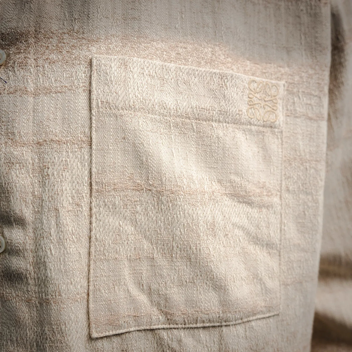 Beige shirt chest pocket with stitched panel and button area.