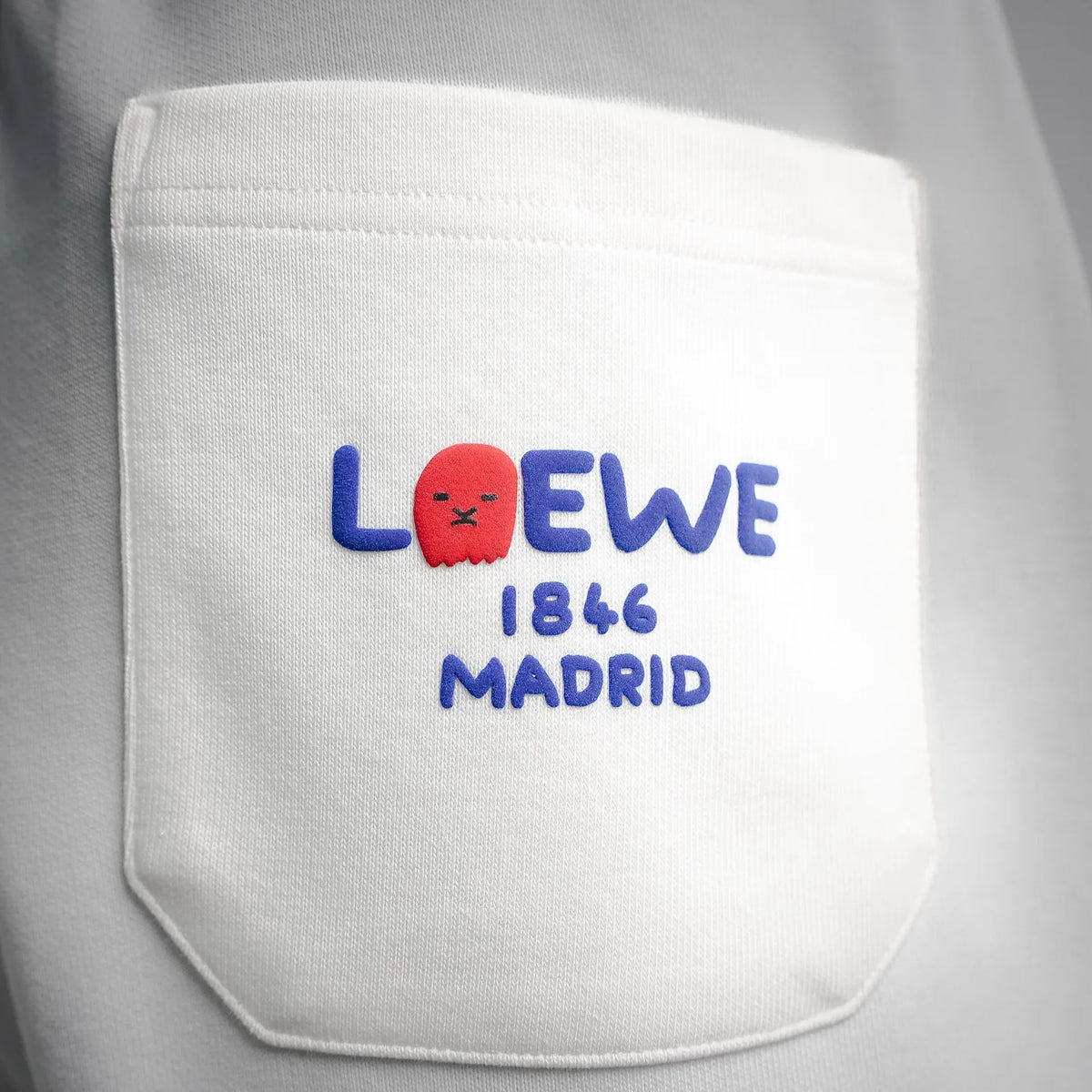 LOEWE logo patch on white shorts: red animal, blue text, Madrid 1846