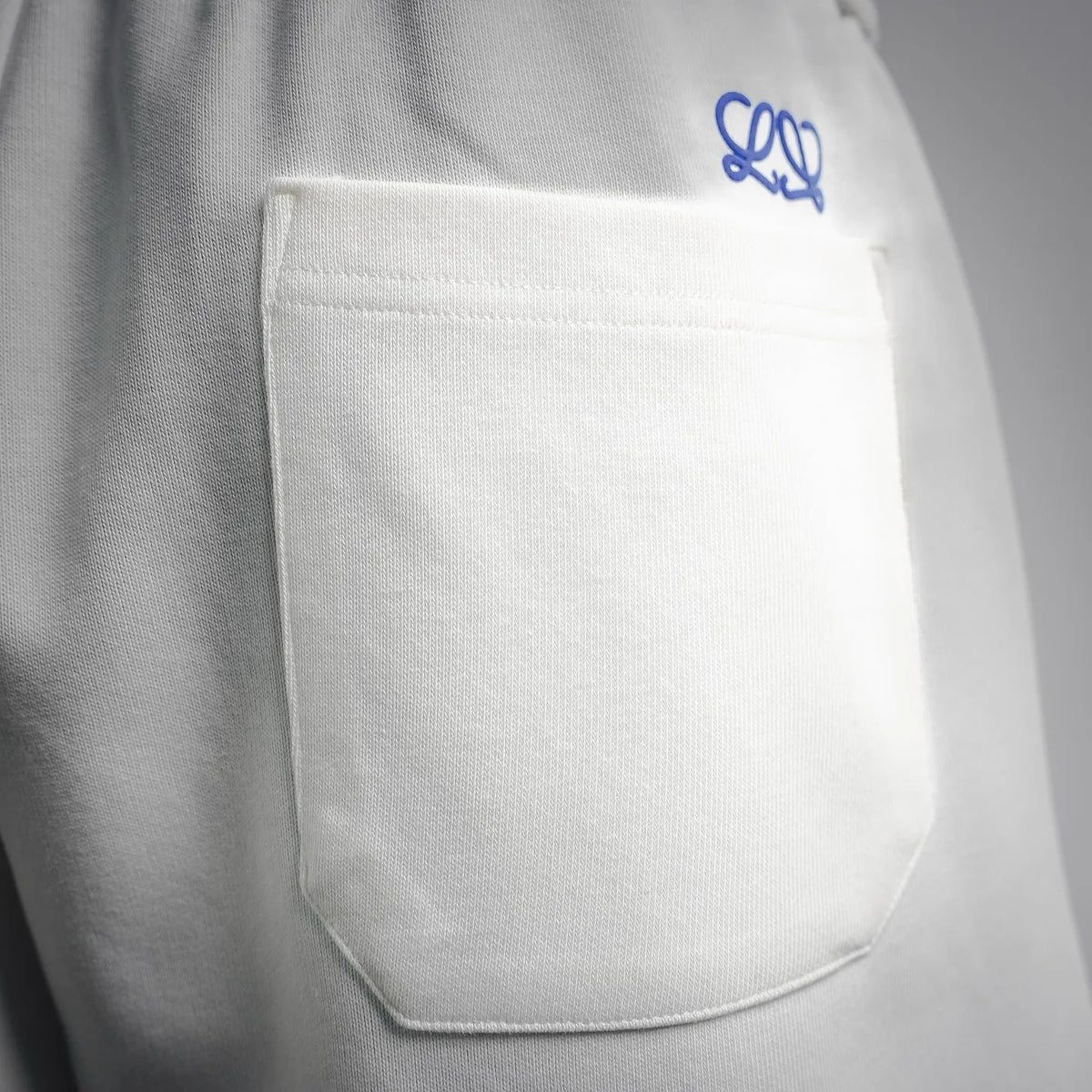 White LOEWE shorts front pocket with blue embroidered logo above the pocket.
