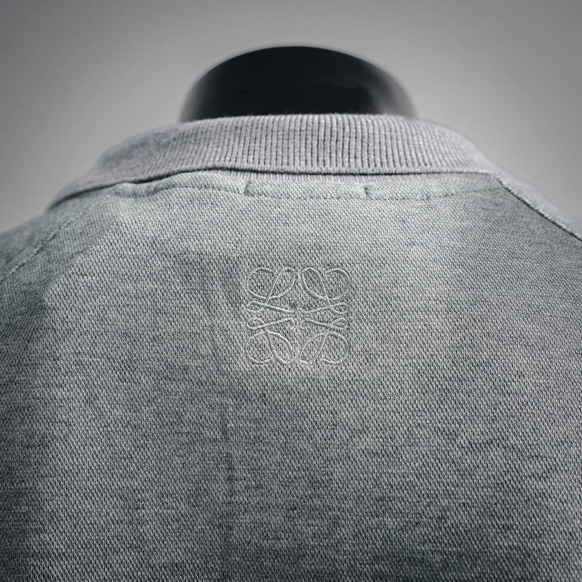Heather gray polo shirt back with subtle embossed logo near the neckline