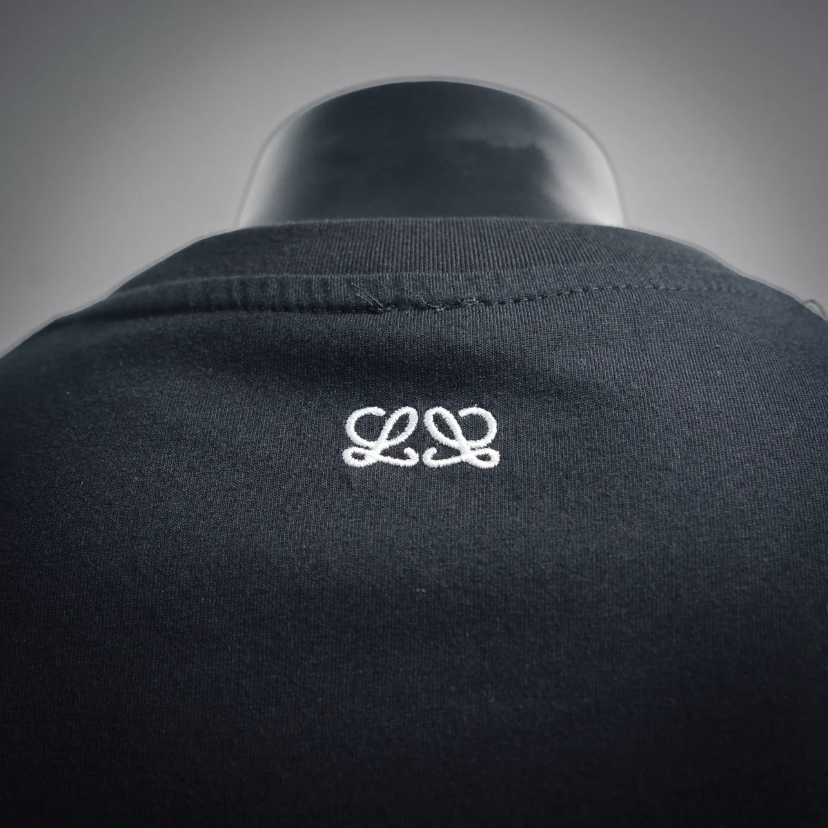Dark T-shirt fabric close-up with small white LOEWE logo on upper back