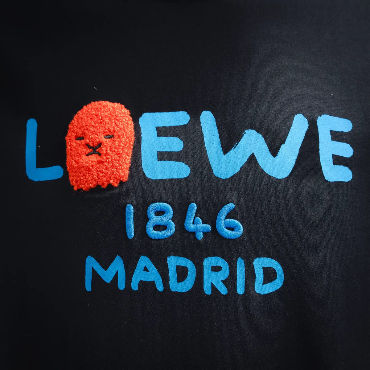 Black T-shirt close-up of colorful LOEWE 1846 Madrid logo print