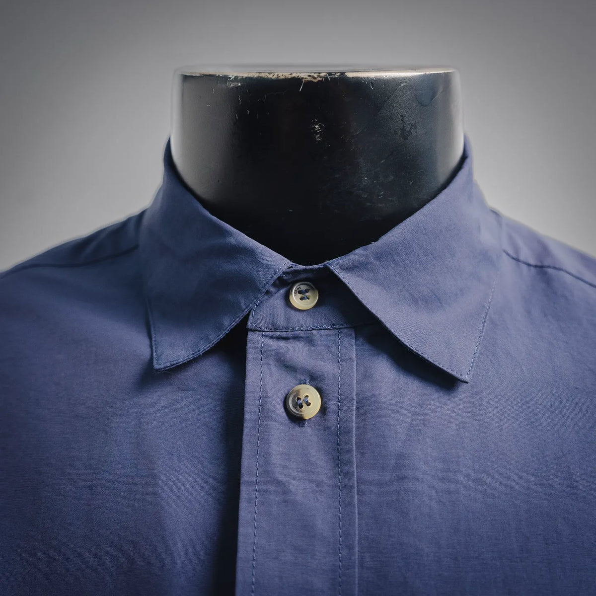Blue short-sleeve button-up shirt with open collar and two visible gold buttons.
