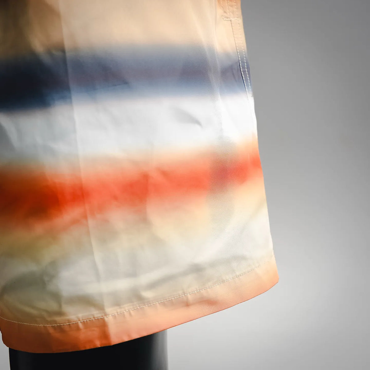 Side view of tie-dye swim shorts hem with orange border trim