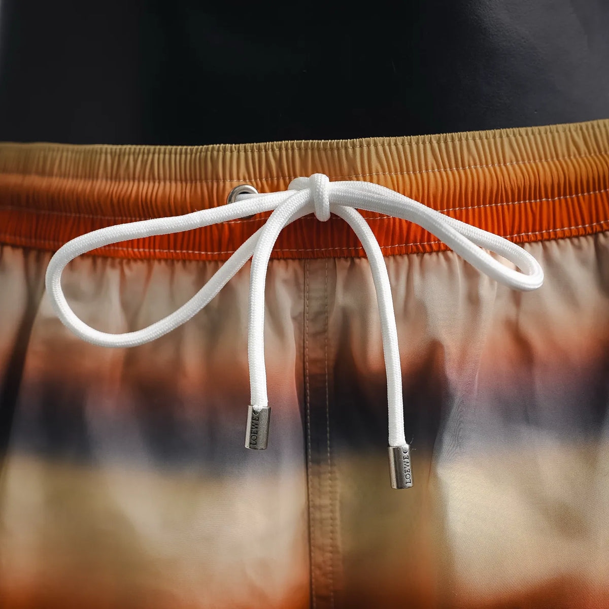 Drawstring cords on tie-dye swim shorts with knot and metal ends