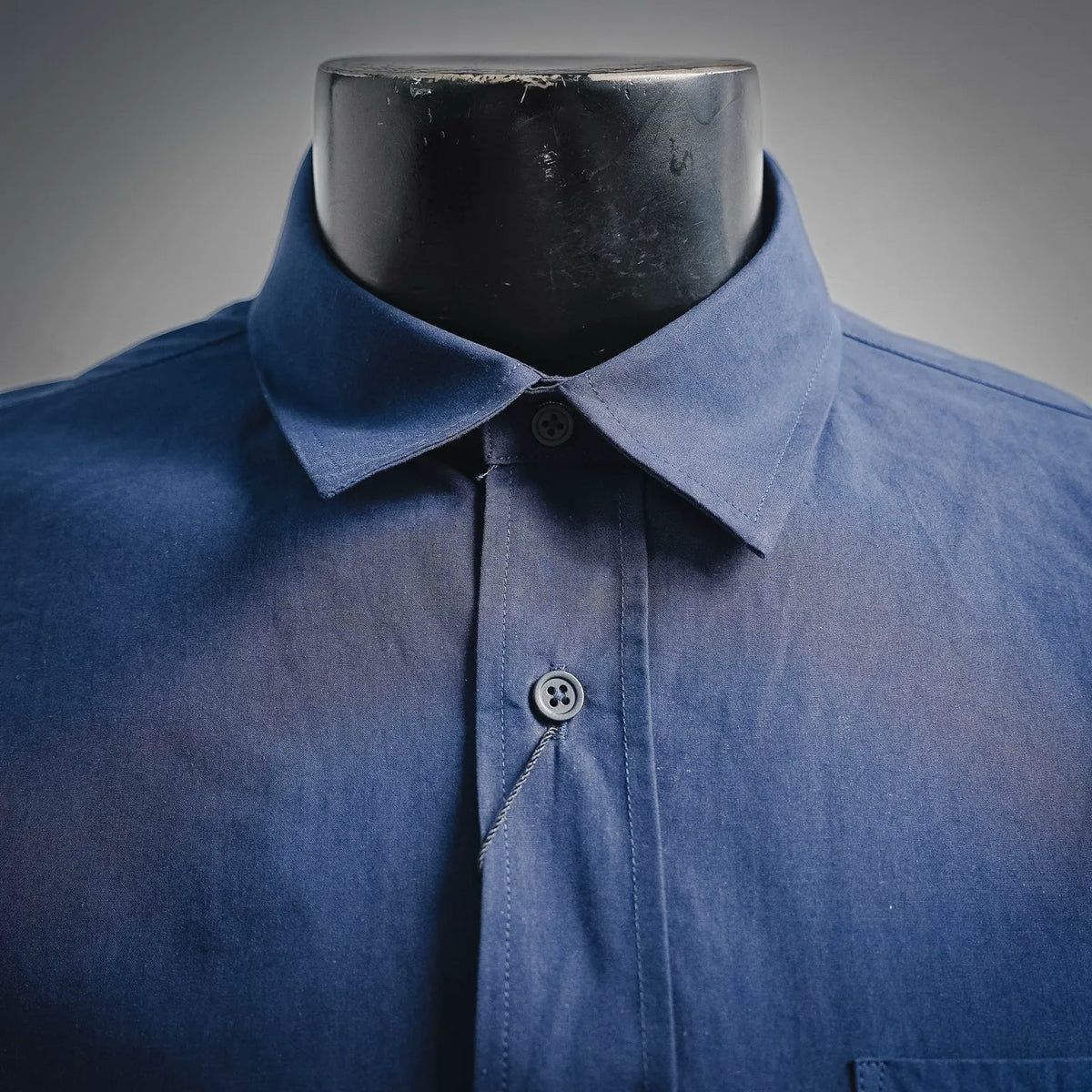 Blue dress shirt collar with button placket and small chest emblem patch.