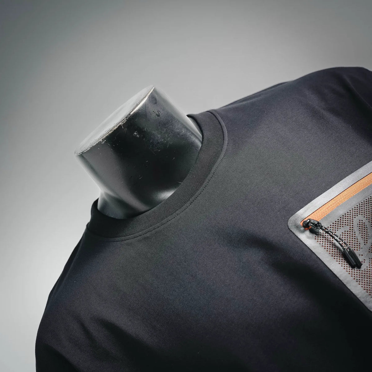Black T-shirt neckline with orange-trim patch pocket detail.