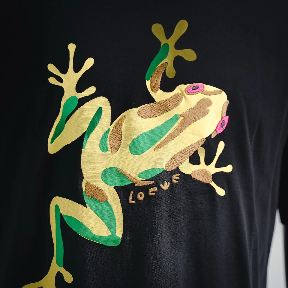 Black T-shirt close-up of front graphic dinosaur lizard illustration in beige and green