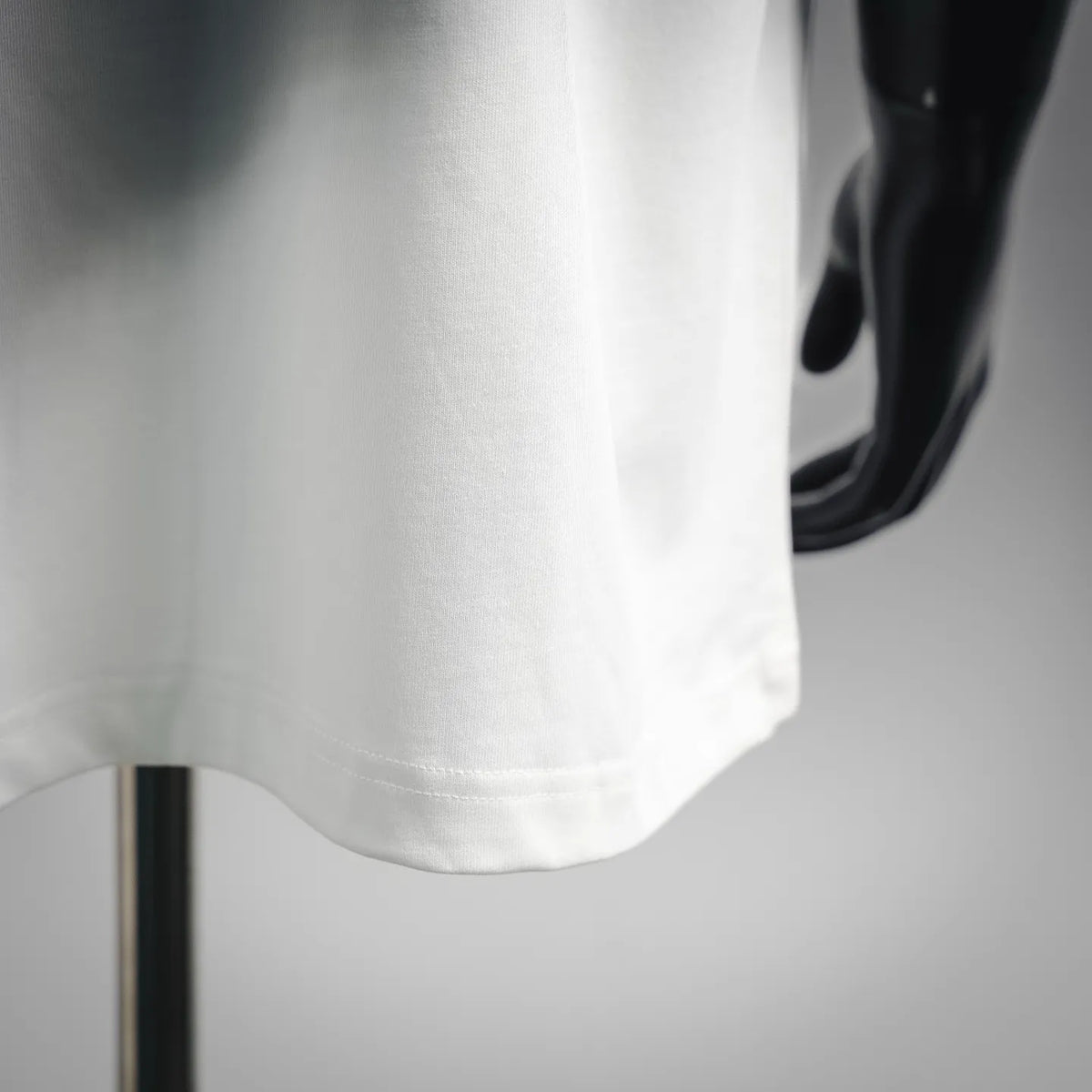 White T-shirt hem detail, short sleeve edge and stitching visible on mannequin.