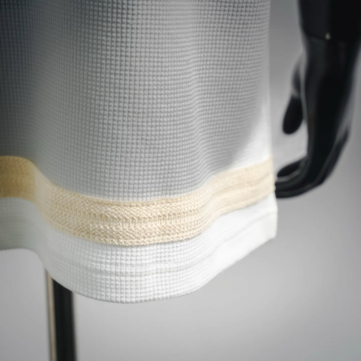Close-up of white waffle-knit T-shirt hem with beige trim