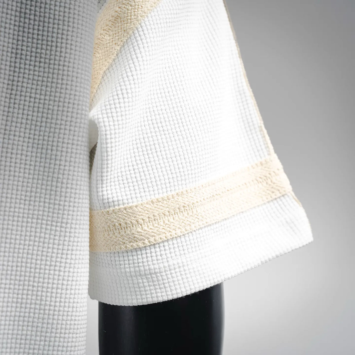 Close-up of white sleeve and hem with beige striped band