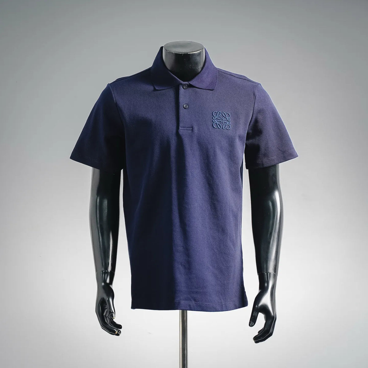 Dark blue short-sleeve polo shirt on mannequin, buttoned collar and chest emblem