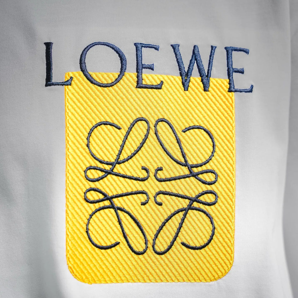 LOEWE chest graphic patch: yellow square with blue lettering and black line art