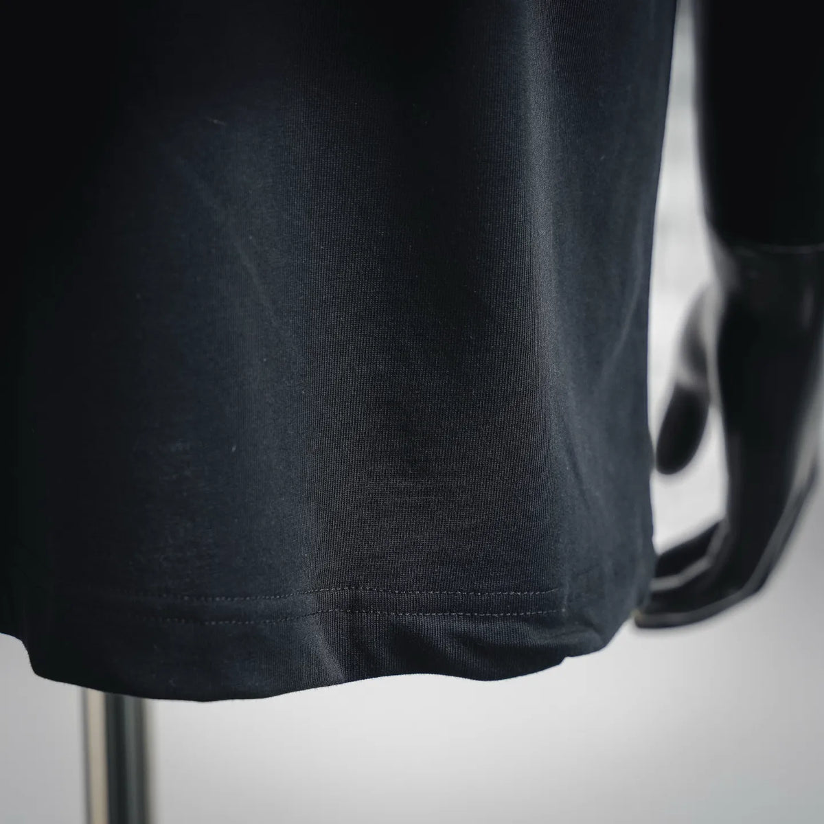 Black T-shirt hem and stitched seam, close-up on mannequin.