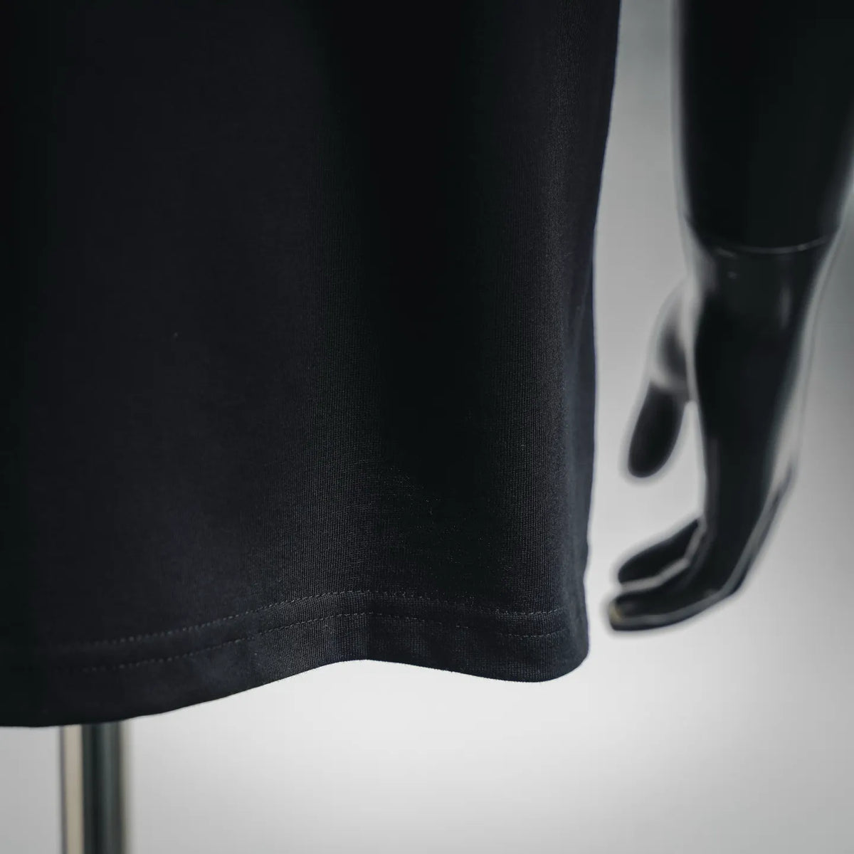 Black T-shirt fabric close-up with stitched hem and curved lower edge.
