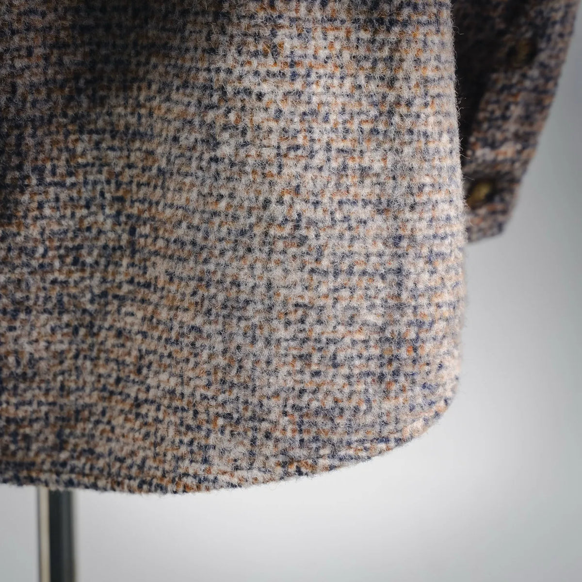 Beige tweed fabric close-up with blue-brown flecked weave texture.
