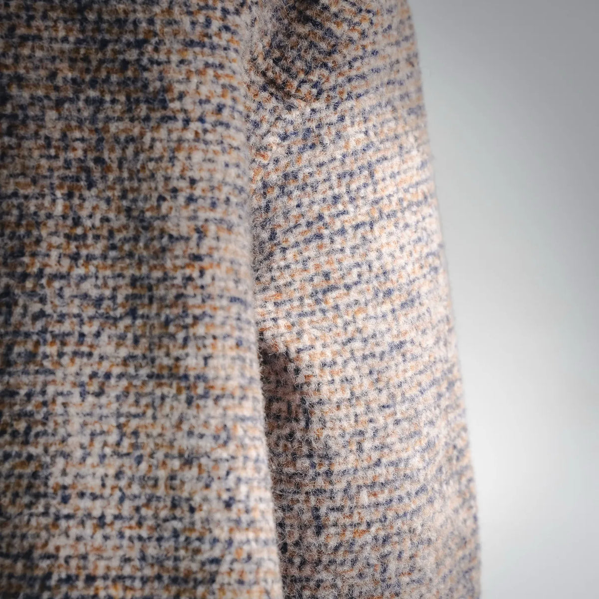 Beige tweed coat sleeve close-up showing seam and textured weave.