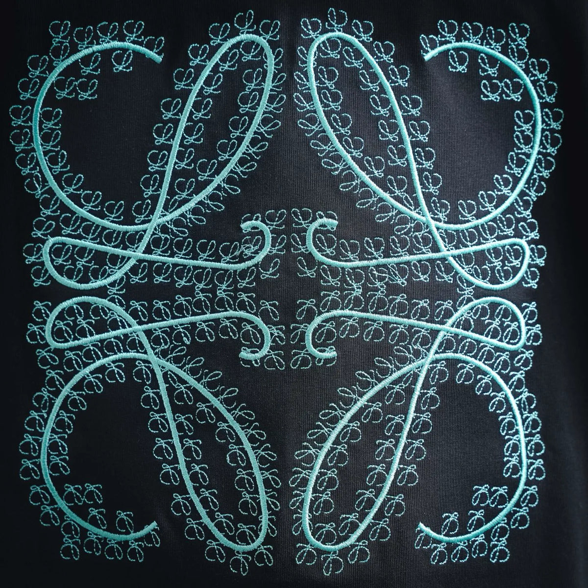 Turquoise embroidered monogram detail on a black short-sleeve T-shirt