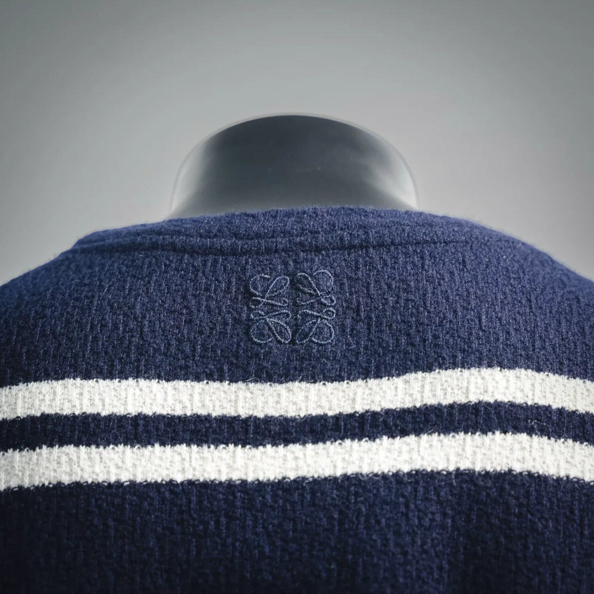 Back of navy knit sweater with LOEWE monogram stitch above white stripe bands