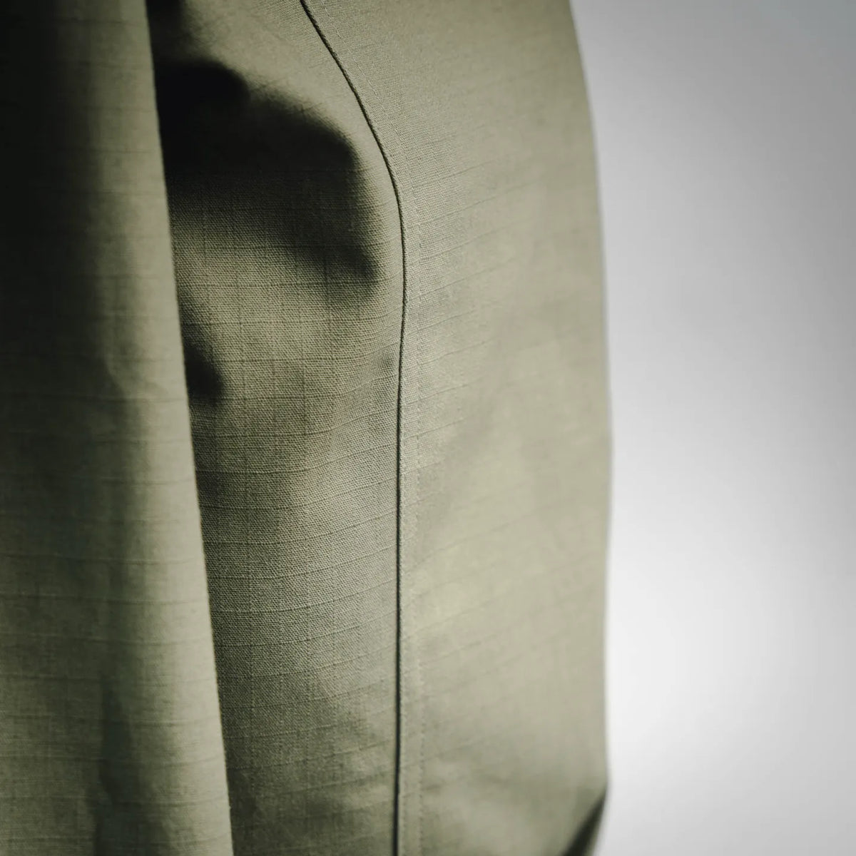 Olive green coat side with curved pocket seam and vertical stitching detail