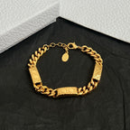 Gold-tone chain bracelet with textured links and small pendant charm, on black fabric