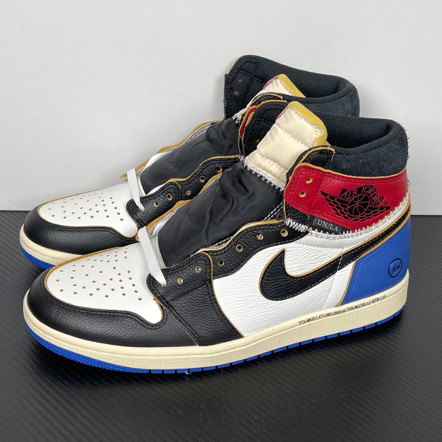 High-top sneaker angle view: black and white leather, red and cream ankle panels, blue outsole