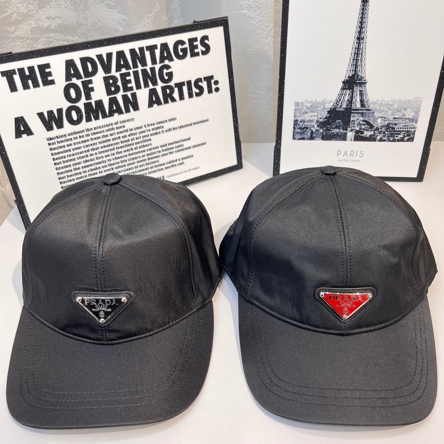 Pair of Prada caps in dark fabric with triangular logo patches, front views.